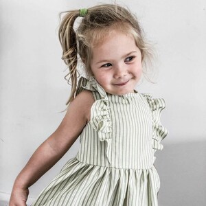 May include: A light green and white striped dress with ruffled sleeves. The dress is sleeveless and has a gathered skirt. The child is wearing a green hair tie.