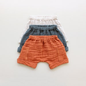 May include: Three pairs of cotton shorts in different colors: orange, gray, and white. The shorts have a relaxed fit and are made of a soft, breathable fabric.