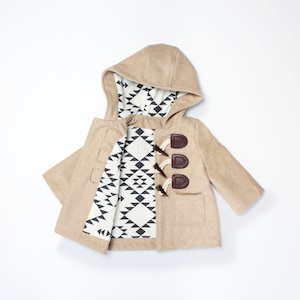 Puede incluir: Un abrigo de color beige para ni&ntilde;os peque&ntilde;os con capucha y forro de estampado geom&eacute;trico. El abrigo tiene un cierre de bot&oacute;n de cuero marr&oacute;n.