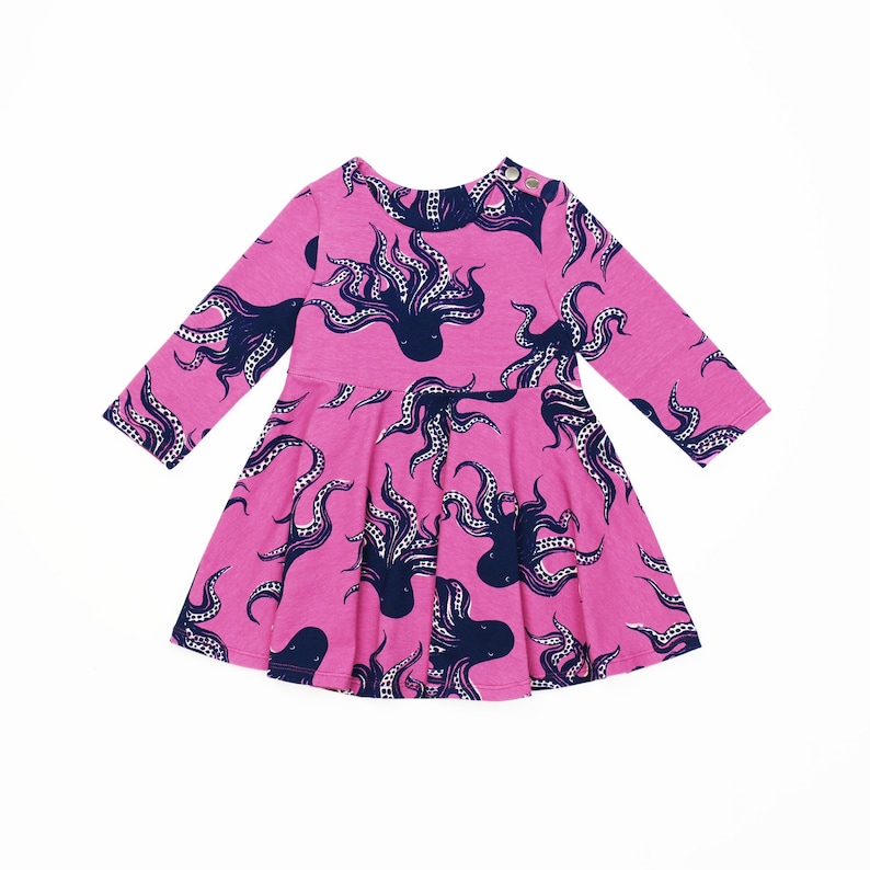 May include: A pink long-sleeved dress with a pattern of blue octopus silhouettes. The dress has a round neckline and a flared skirt.