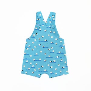 May include: Light blue baby overalls with a white sheep pattern. The overalls have adjustable straps with metal buckles.