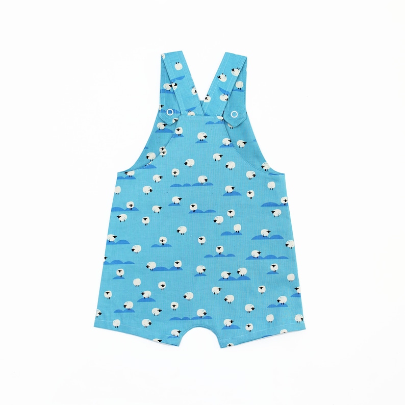 May include: Light blue baby overalls with a white sheep pattern. The overalls have adjustable straps with metal buckles.