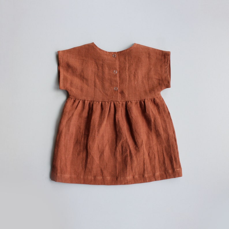 May include: A rust-colored linen dress with short sleeves and a button closure in the back.