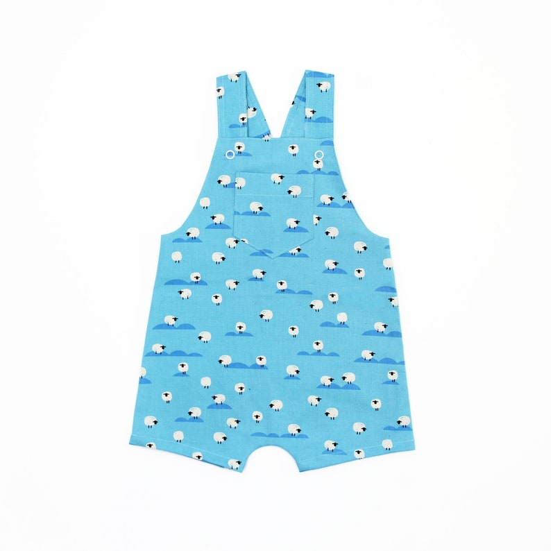 May include: Light blue baby overalls with a white sheep print. The overalls have two pockets and adjustable straps.