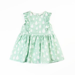 May include: A mint green baby dress with a white raindrop pattern. The dress features ruffled sleeves and a gathered skirt. The dress is sleeveless and has a button closure at the back of the neck.