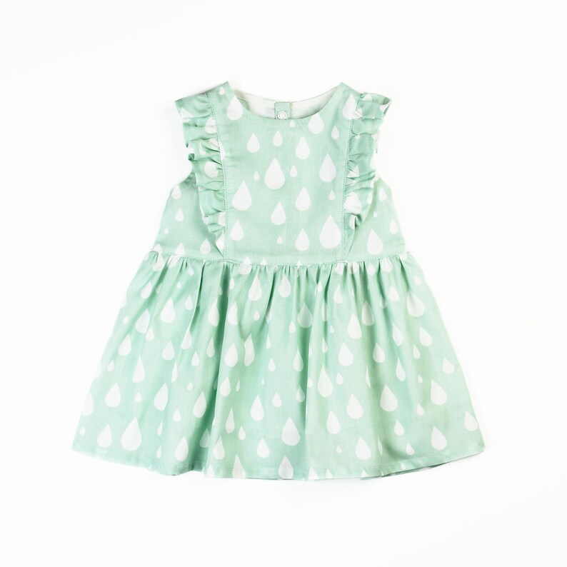 May include: A mint green baby dress with a white raindrop pattern. The dress features ruffled sleeves and a gathered skirt. The dress is sleeveless and has a button closure at the back of the neck.