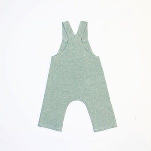 May include: A light green baby overall with adjustable straps and a relaxed fit.