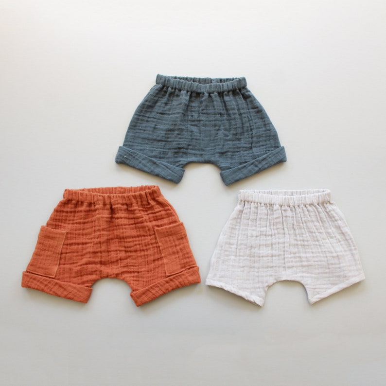 May include: Three pairs of baby shorts in different colors: blue, orange, and white. The shorts are made of a soft, lightweight fabric and have a relaxed fit.