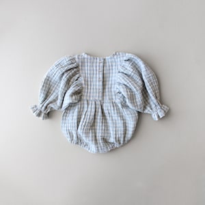 May include: A blue and white gingham baby onesie with puffed sleeves and a button closure down the back.