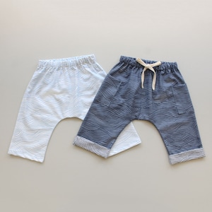 May include: Two pairs of baby pants with a wave pattern. One pair is light blue with white waves, and the other pair is dark blue with white waves.