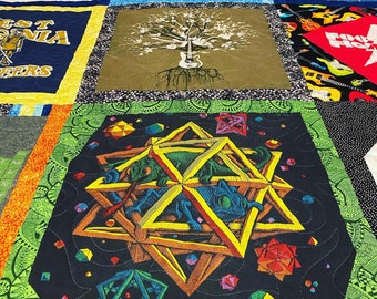 May include: A quilt with a variety of colorful fabrics and patterns. The center panel features a black background with a geometric design in shades of orange, yellow, and green. The design resembles a stylized star or flower.