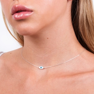 May include: A silver chain necklace with a small blue evil eye charm. The necklace is delicate and simple, making it a perfect everyday accessory.