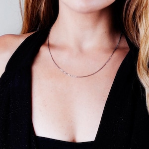 May include: A delicate silver chain necklace worn by a person with long brown hair.