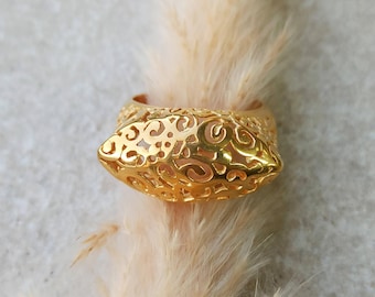 May include: A gold ring with an openwork design. The ring has an elongated, oval-shaped centerpiece with intricate cut-out patterns. The band and the centerpiece are decorated with swirling and floral-like motifs, creating a delicate and ornate appearance.