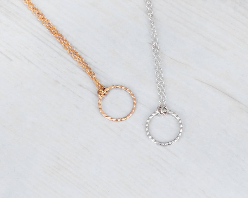 Puede incluir: Dos delicados collares con eslabones de cadena retorcidos y un simple colgante circular. Un collar es dorado y el otro es plateado.