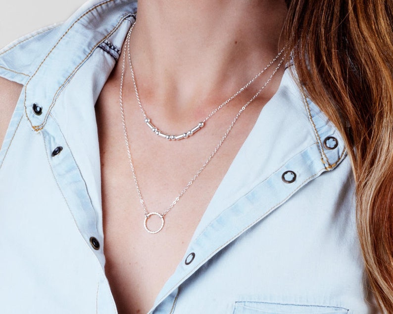Puede incluir: Un collar de plata con un delicado colgante circular y una fila de peque&ntilde;as cuentas de plata.