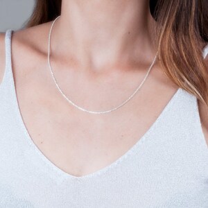 May include: A silver chain necklace on a person wearing a white top.