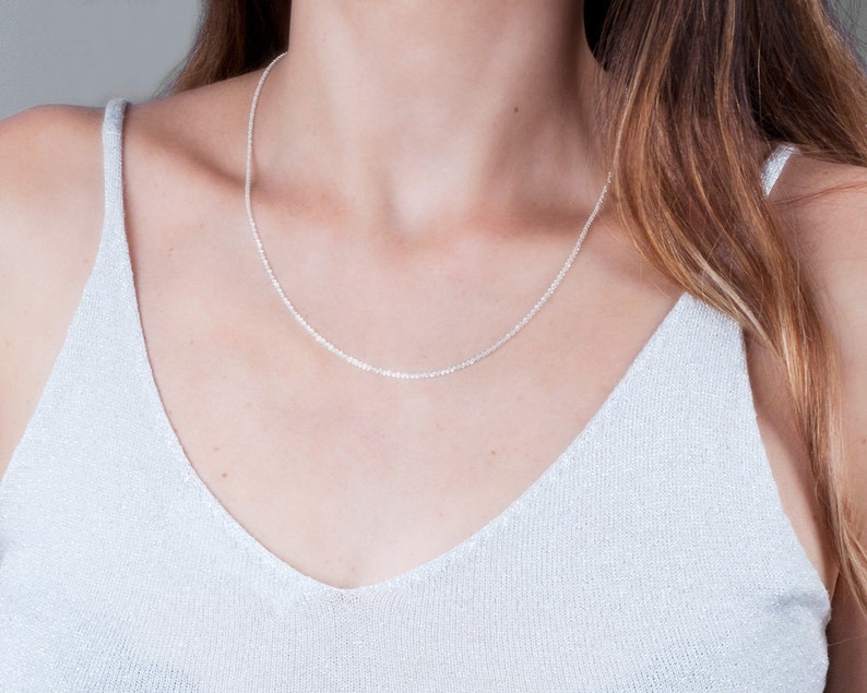 May include: A silver chain necklace on a person wearing a white top.