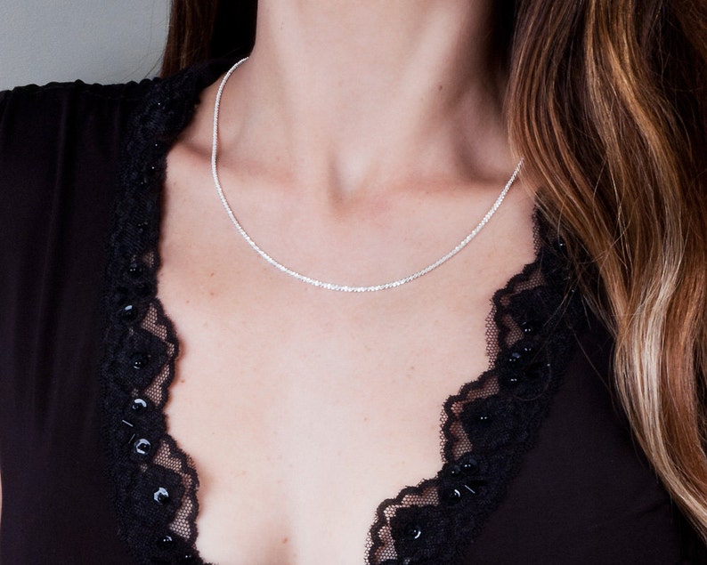 May include: A silver chain necklace on a model wearing a black top with lace trim.
