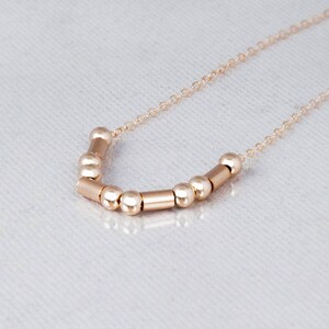 Puede incluir: Un collar de oro con una cadena delicada y una fila de cuentas y cilindros de oro alternados.