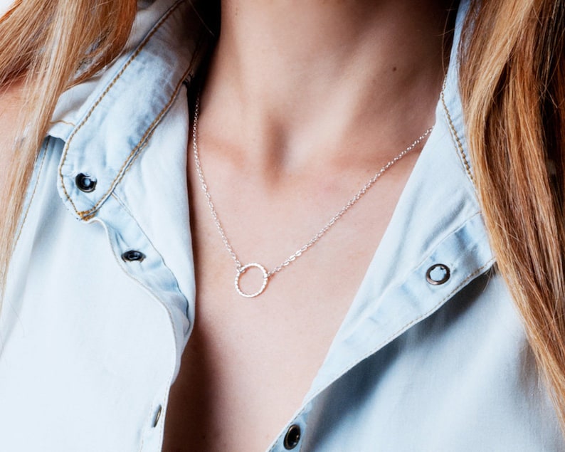 Puede incluir: Un collar de plata con un colgante circular texturizado.