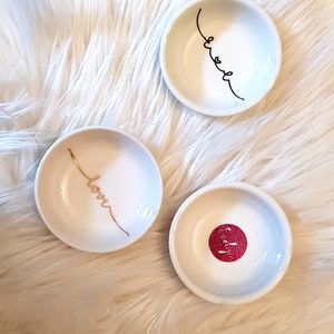 May include: Three small white ceramic dishes with gold and black lettering. The dishes say "love", "sweet", and "pretty".