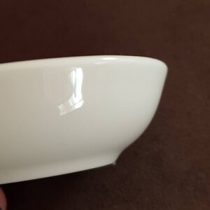 May include: A white ceramic bowl with a smooth, glossy finish. The bowl is slightly curved and has a rounded bottom.