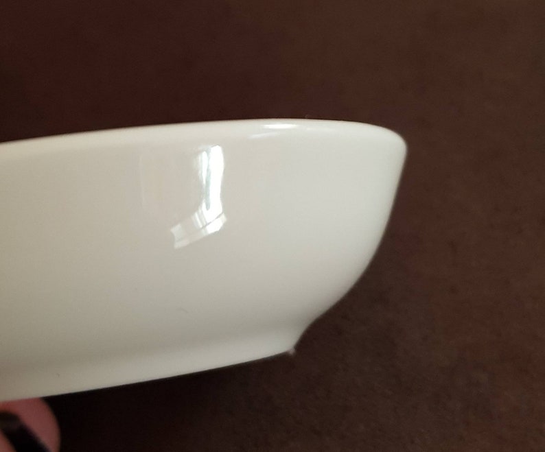 May include: A white ceramic bowl with a smooth, glossy finish. The bowl is slightly curved and has a rounded bottom.
