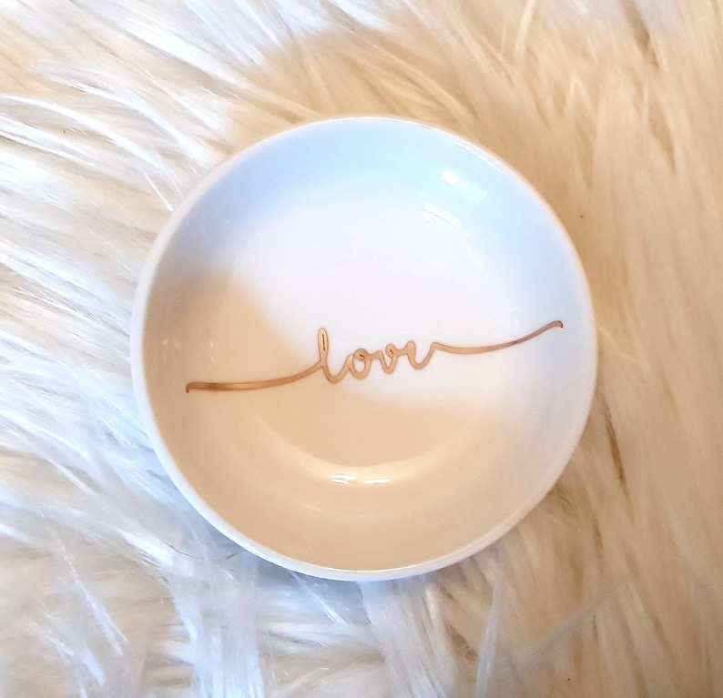 May include: A white ceramic ring dish with a gold inscription that reads "love".