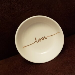 May include: White ceramic trinket dish with a gold cursive inscription that reads "love".