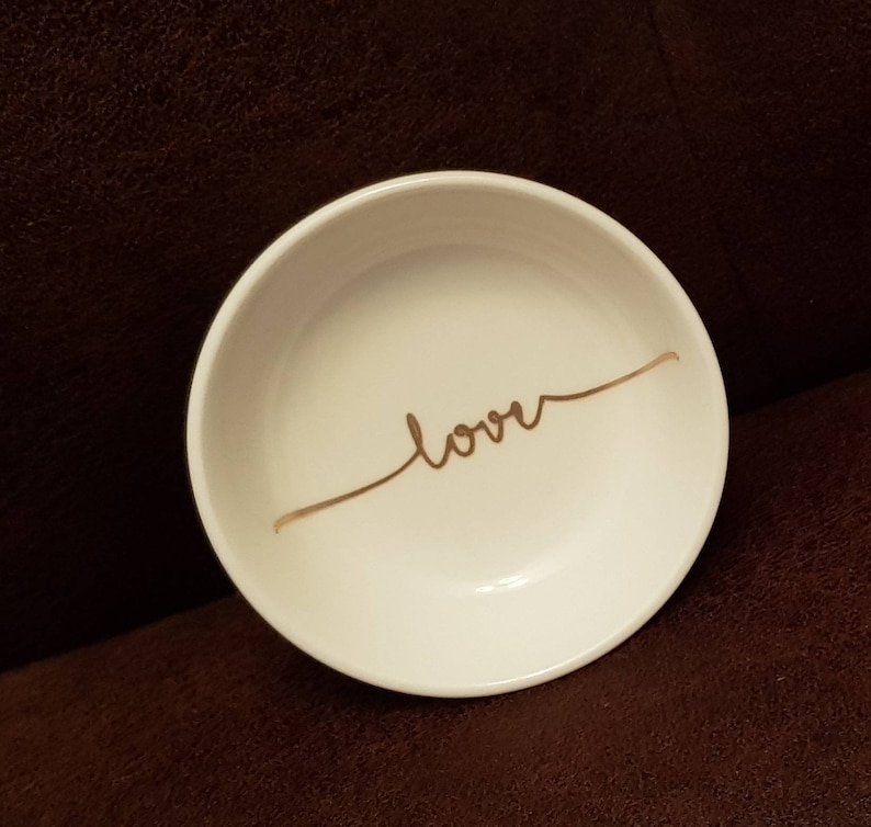 May include: White ceramic trinket dish with a gold cursive inscription that reads "love".