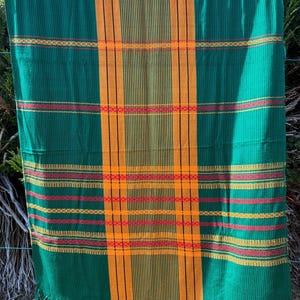 Peut inclure: Textile tissé vert et orange avec une bordure à franges. Le textile présente des rayures verticales orange et des rayures horizontales rouges, jaunes et orange. Le textile est suspendu à l'extérieur.