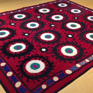 K&ouml;nnte beinhalten: Ein roter Stoffteppich mit einem sich wiederholenden Muster aus schwarzen, wei&szlig;en und gr&uuml;nen Kreisen. Die Kreise haben ein stilisiertes Blumenmuster um sie herum.