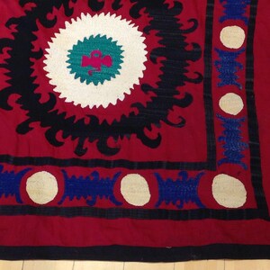K&ouml;nnte beinhalten: Ein rotes, schwarzes und wei&szlig;es besticktes Textil mit einem geometrischen Muster. Das Textil hat einen Rand aus blauen und wei&szlig;en Kreisen.