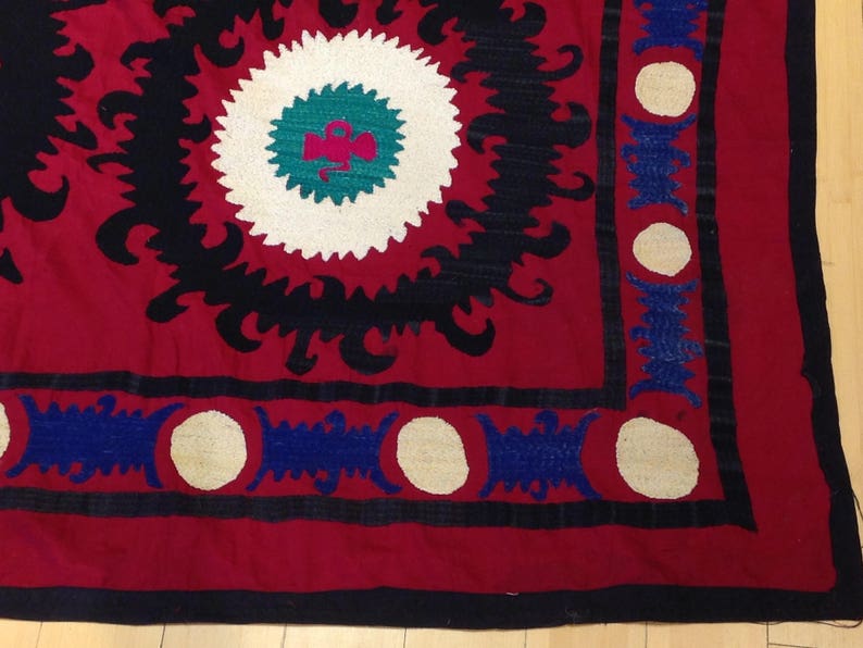 K&ouml;nnte beinhalten: Ein rotes, schwarzes und wei&szlig;es besticktes Textil mit einem geometrischen Muster. Das Textil hat einen Rand aus blauen und wei&szlig;en Kreisen.