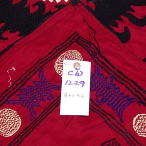 K&ouml;nnte beinhalten: Roter Stoff mit schwarzen und blauen Stickereien. Der Stoff hat ein Etikett mit dem Text "CW 1229 7.6 x 9.2."