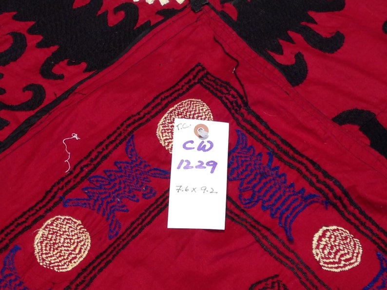 K&ouml;nnte beinhalten: Roter Stoff mit schwarzen und blauen Stickereien. Der Stoff hat ein Etikett mit dem Text "CW 1229 7.6 x 9.2."