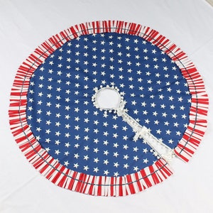 May include: A blue and white American flag patterned Christmas tree skirt with a red and white ruffled trim.