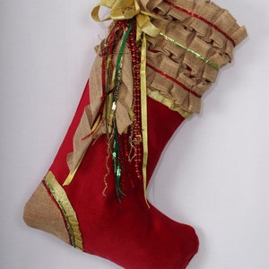 May include: Red Christmas stocking with a brown burlap cuff and gold ribbon. The cuff is decorated with gold and green trim and a bow.