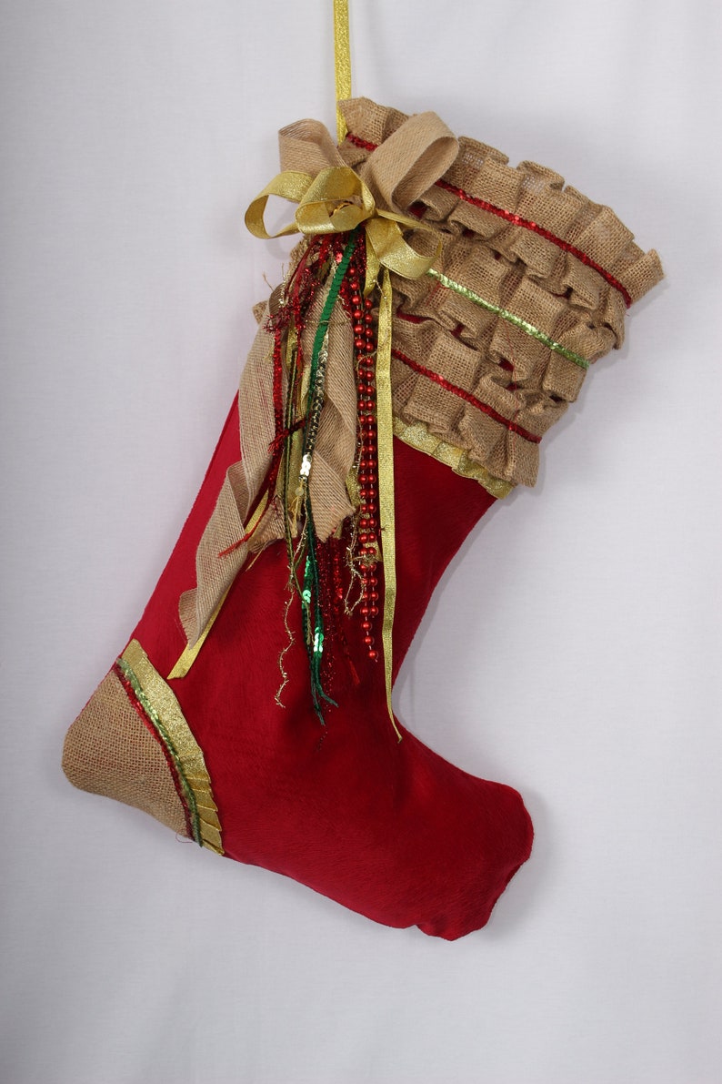 May include: Red Christmas stocking with a brown burlap cuff and gold ribbon. The cuff is decorated with gold and green trim and a bow.