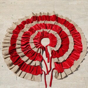 May include: A red and beige circular skirt with multiple layers of fabric. The skirt is made of a soft, flowing material and has a ruffled edge.