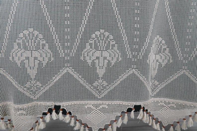 May include: White crocheted curtain with a delicate floral pattern and brown wooden beads along the bottom edge.