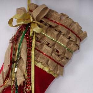 May include: Red Christmas stocking with a burlap ruffle trim, gold ribbon, and green and red beaded garland.