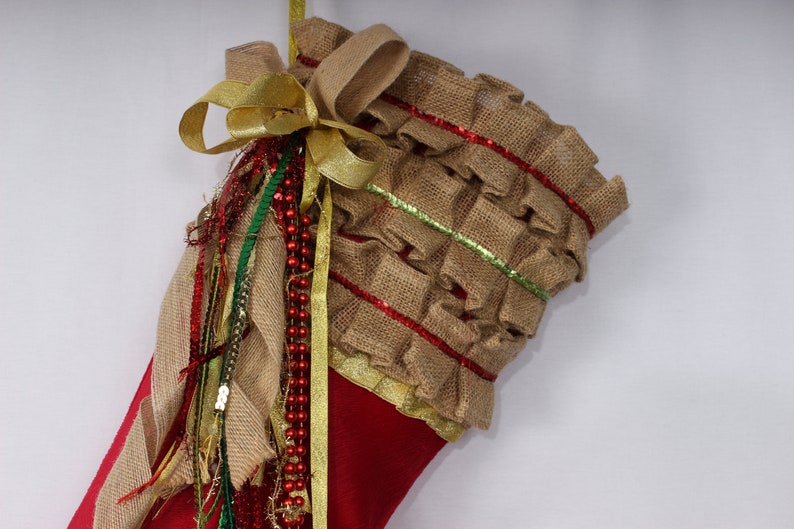 May include: Red Christmas stocking with a burlap ruffle trim, gold ribbon, and green and red beaded garland.