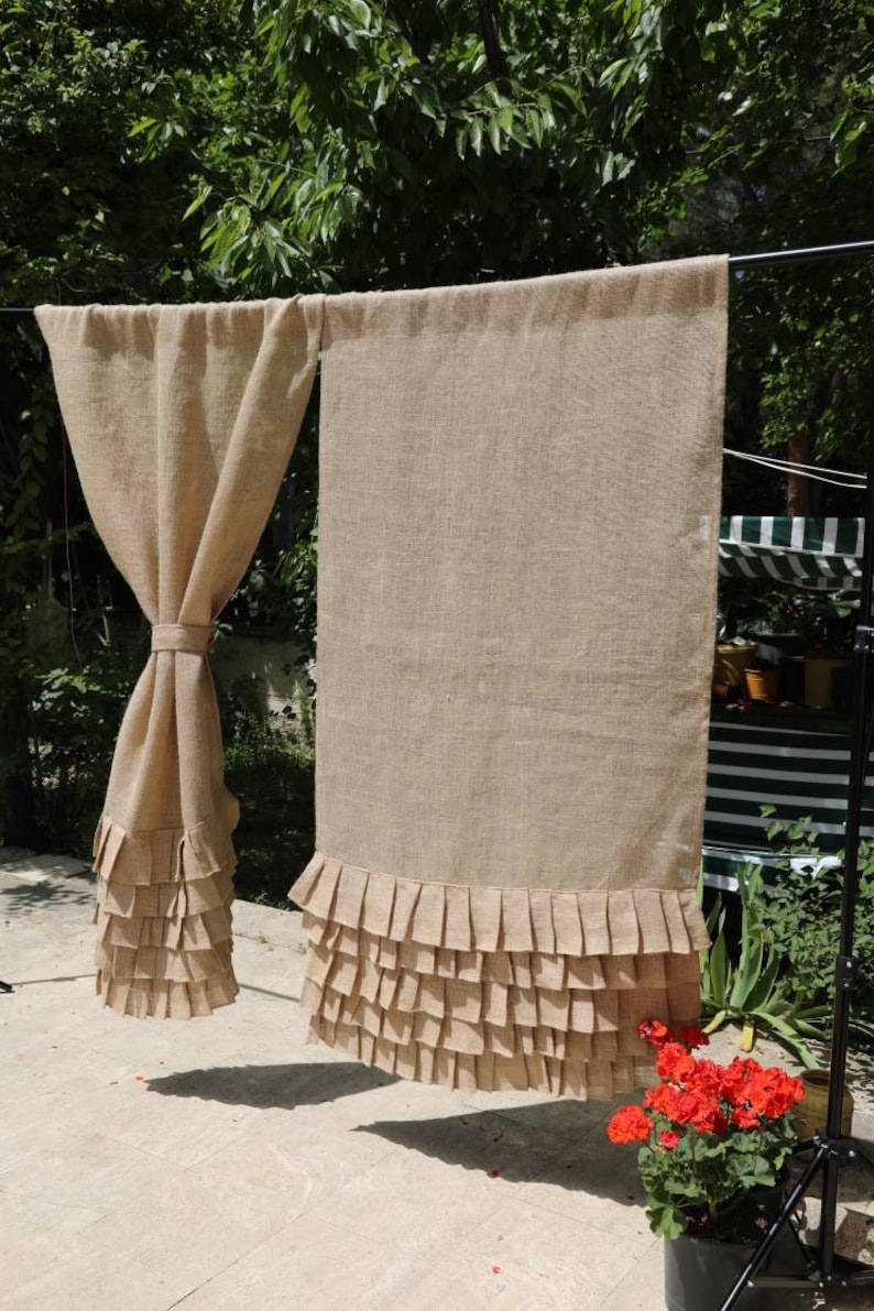 May include: Two brown burlap curtains with a ruffled bottom edge. The curtains are hanging on a black rod.