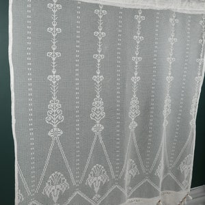 May include: White crocheted curtain panel with a geometric pattern and fringe trim. The curtain is made of a delicate, open-weave fabric.