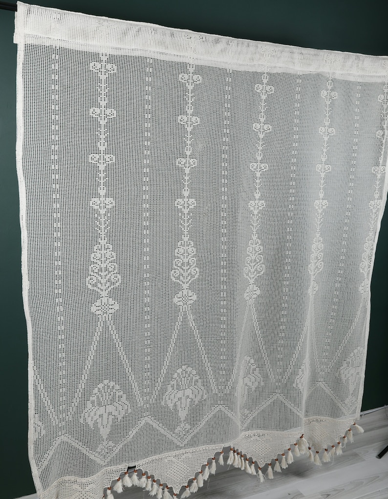 May include: White crocheted curtain panel with a geometric pattern and fringe trim. The curtain is made of a delicate, open-weave fabric.