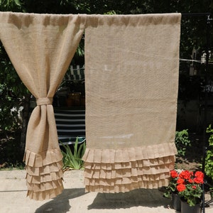May include: Two brown burlap curtains with a ruffled bottom edge. The curtains are hanging from a rod and are in front of a window.