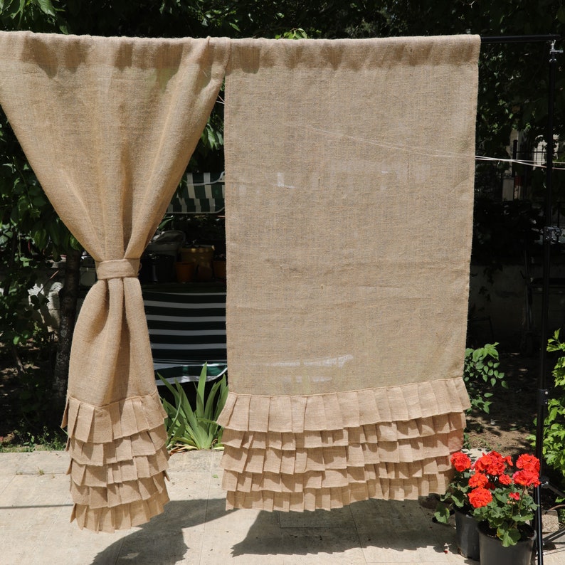 May include: Two brown burlap curtains with a ruffled bottom edge. The curtains are hanging from a rod and are in front of a window.