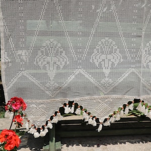 May include: White crocheted curtain with a delicate pattern and tassels along the bottom edge.